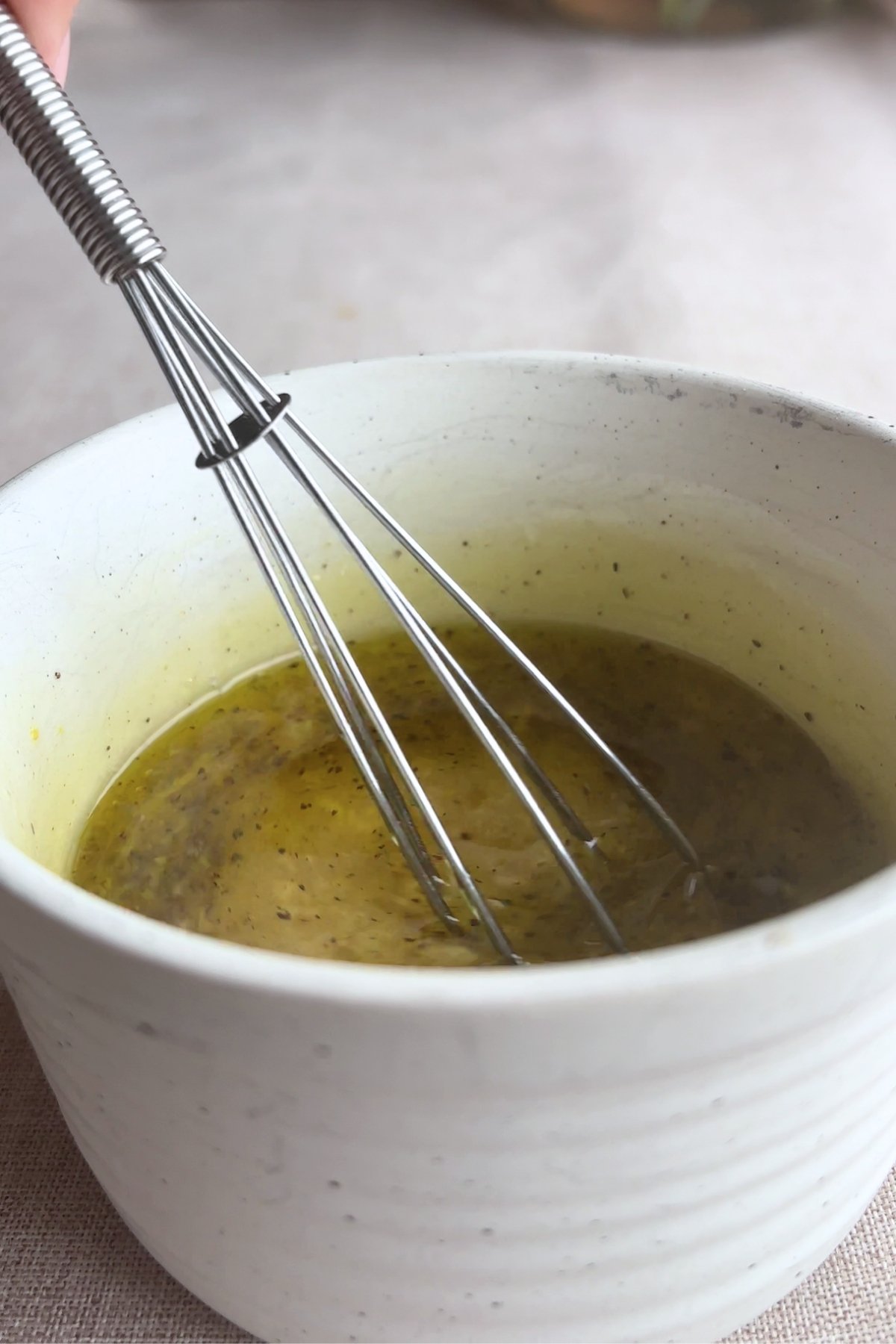 Whisk mixing dressing in a white bowl.
