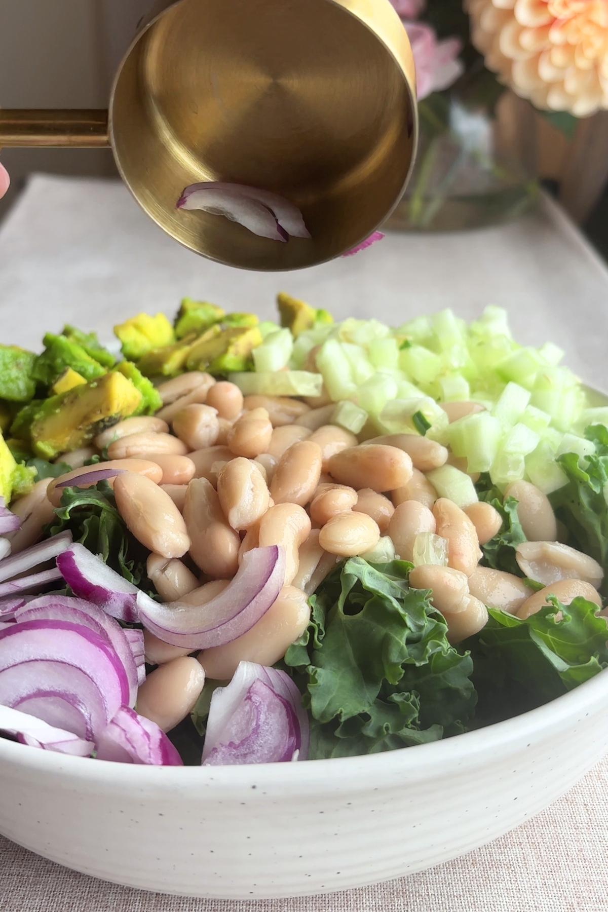 Bowl with kale, white beans, avocado, cucumber, and onion.