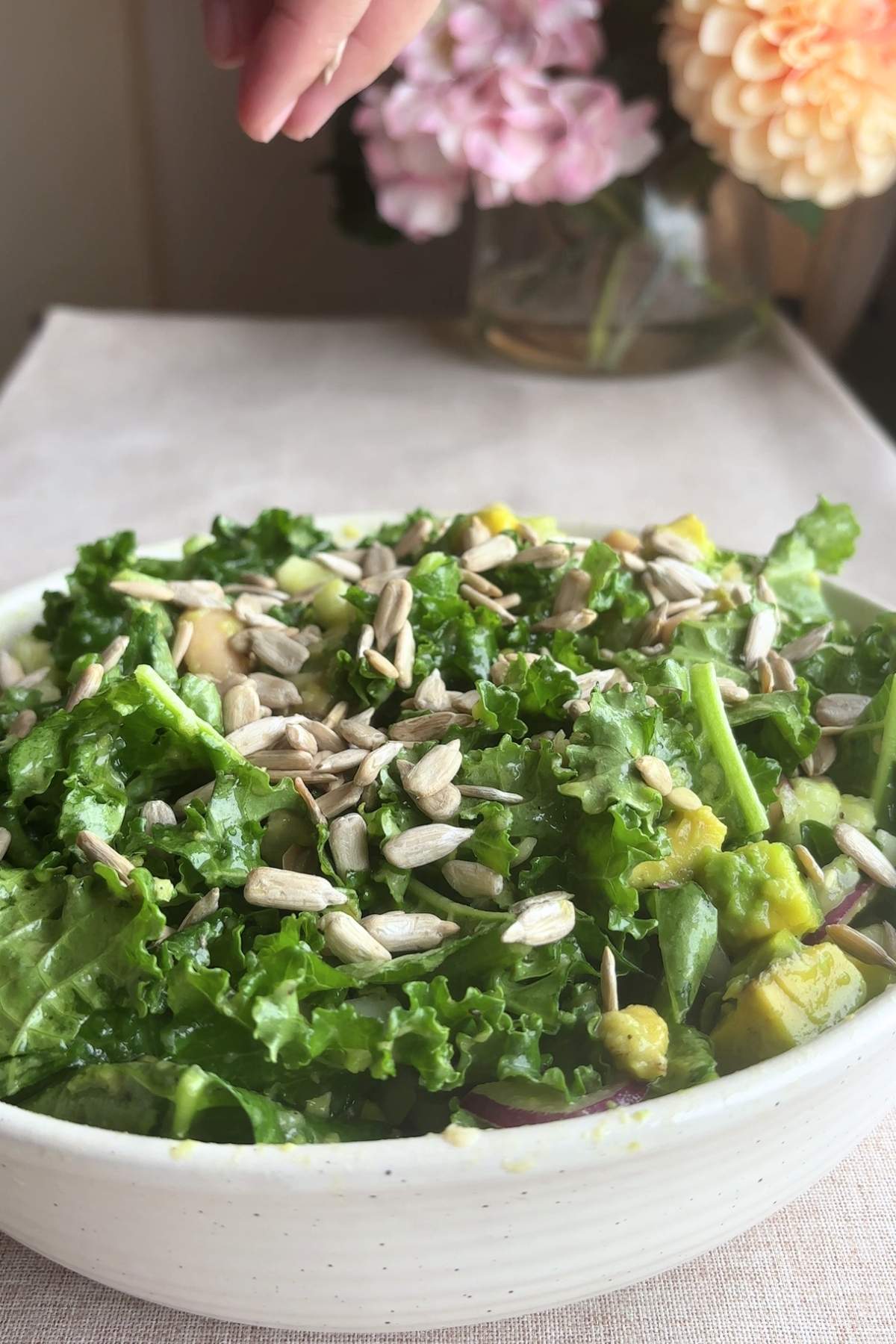 Hand sprinkling sunflower seeds over kale salad.