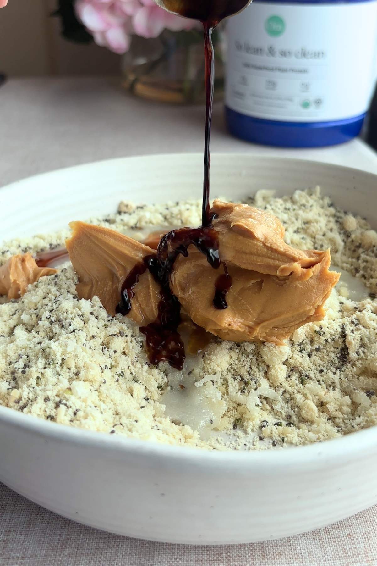 Drizzling syrup over peanut butter in a bowl of dry ingredients.
