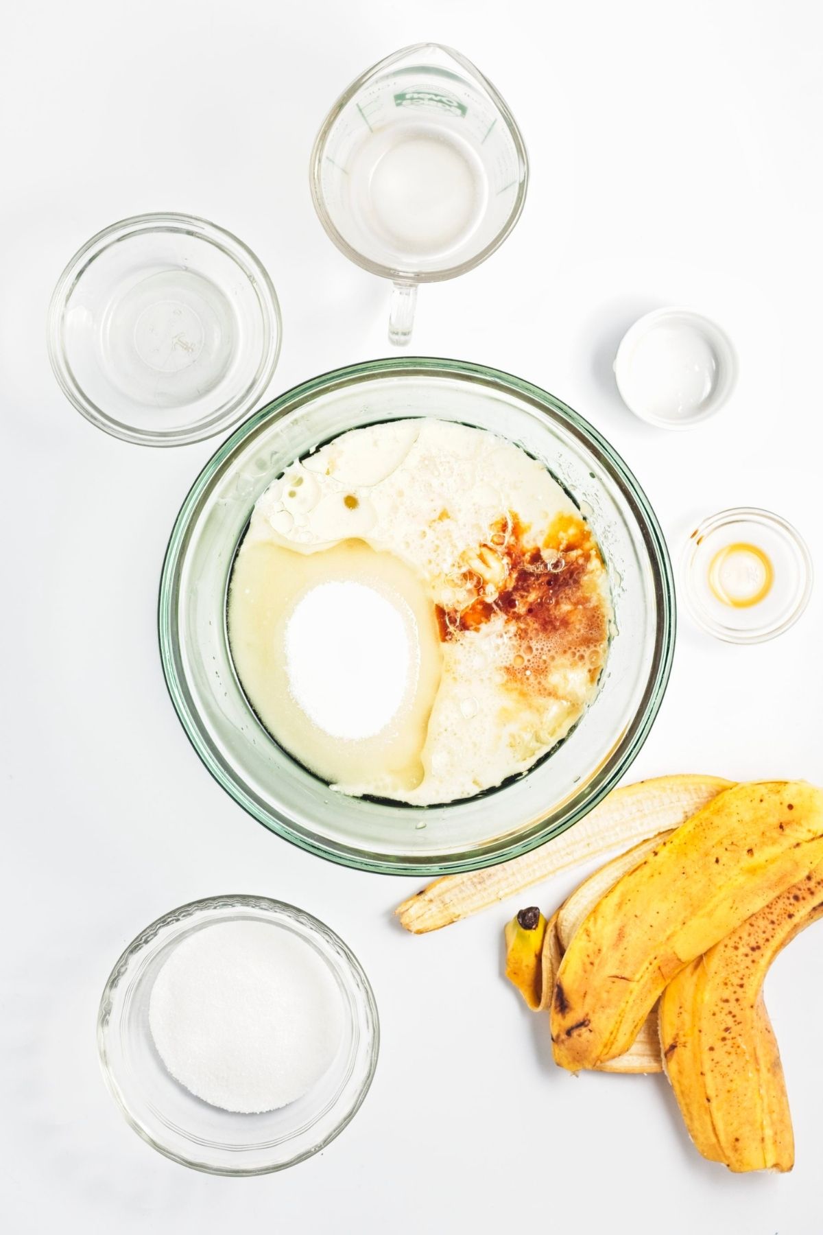 Banana, sugar, oat milk, oil, vanilla, and vinegar combined in a glass mixing bowl.