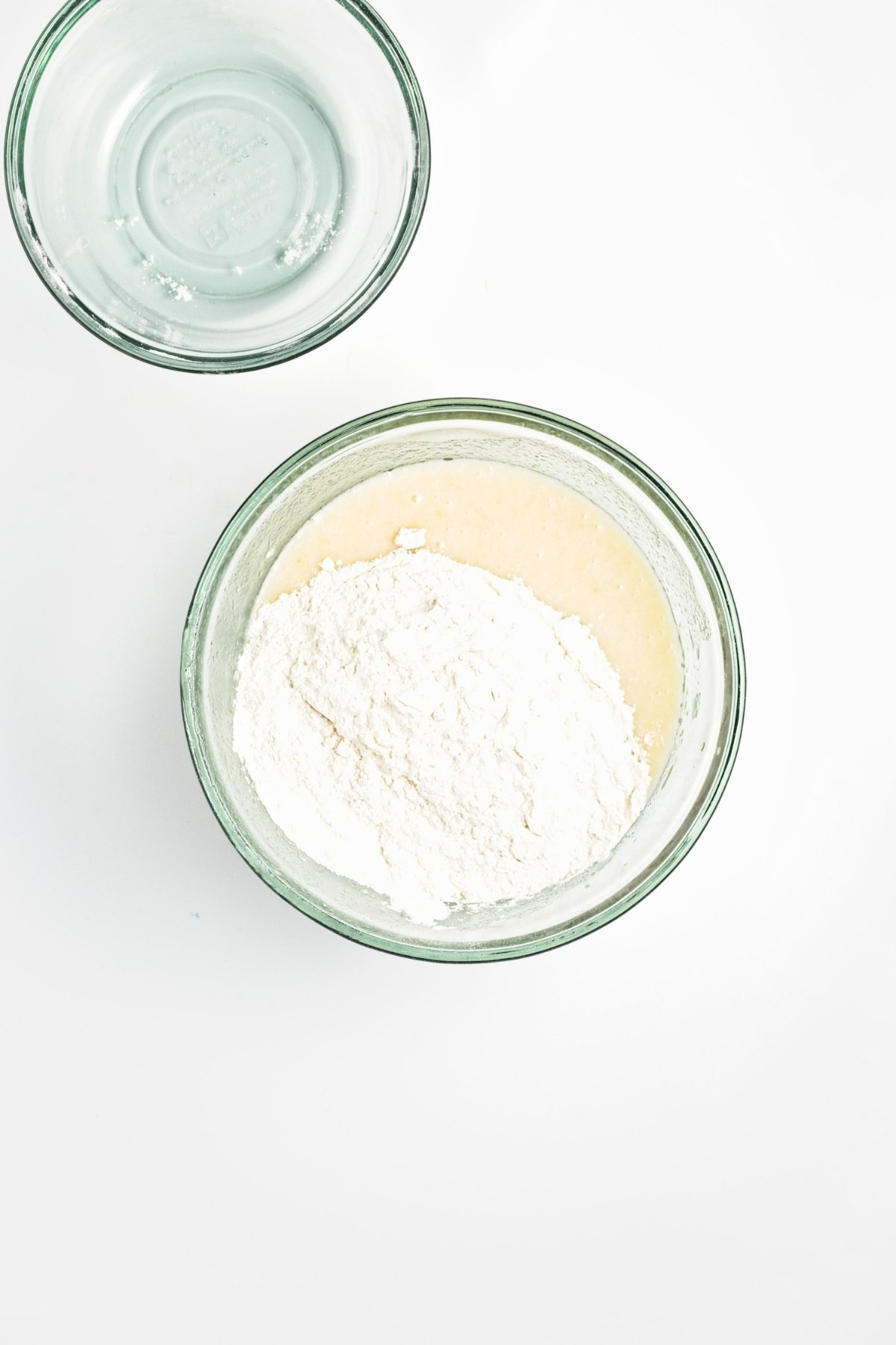 Flour mixture added to wet cupcake batter in a glass mixing bowl.