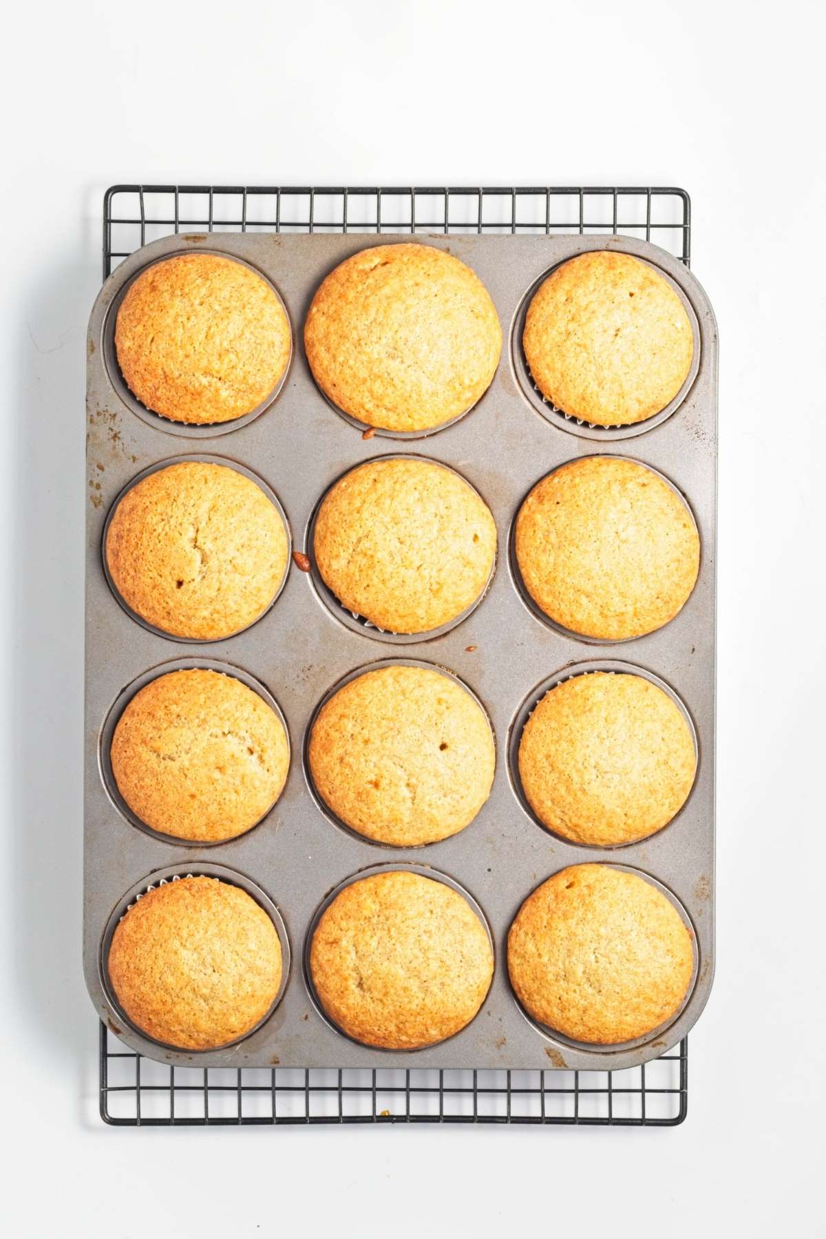 Baked cupcakes cooling in a muffin pan on a wire rack.