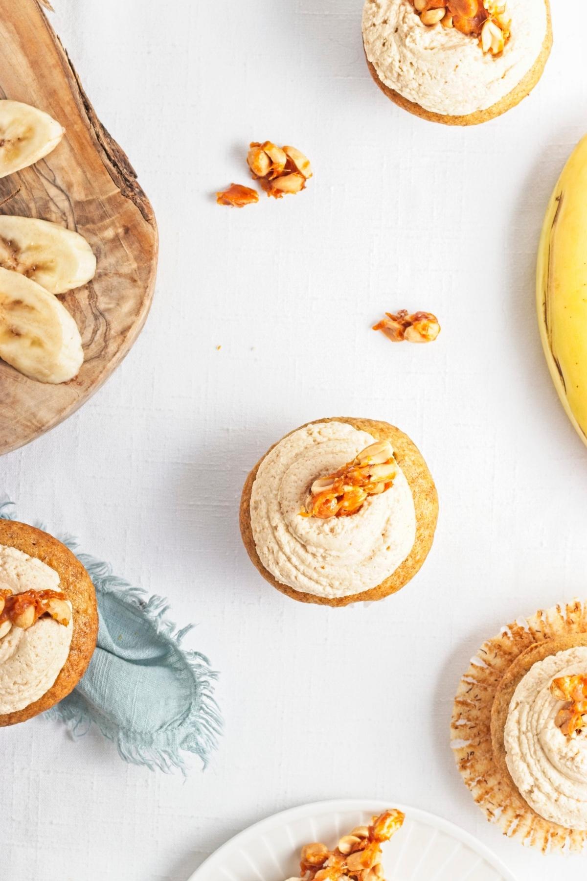 Frosted cupcakes topped with peanut brittle pieces on a white surface.
