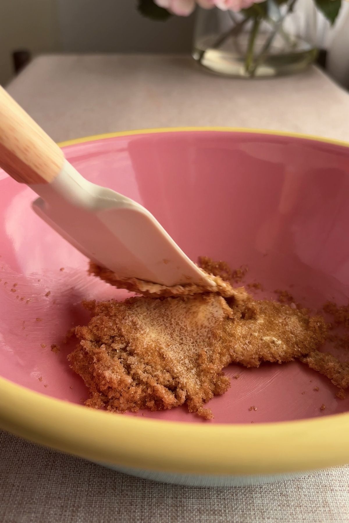 Spatula mixing brown sugar and softened butter in a pink bowl.