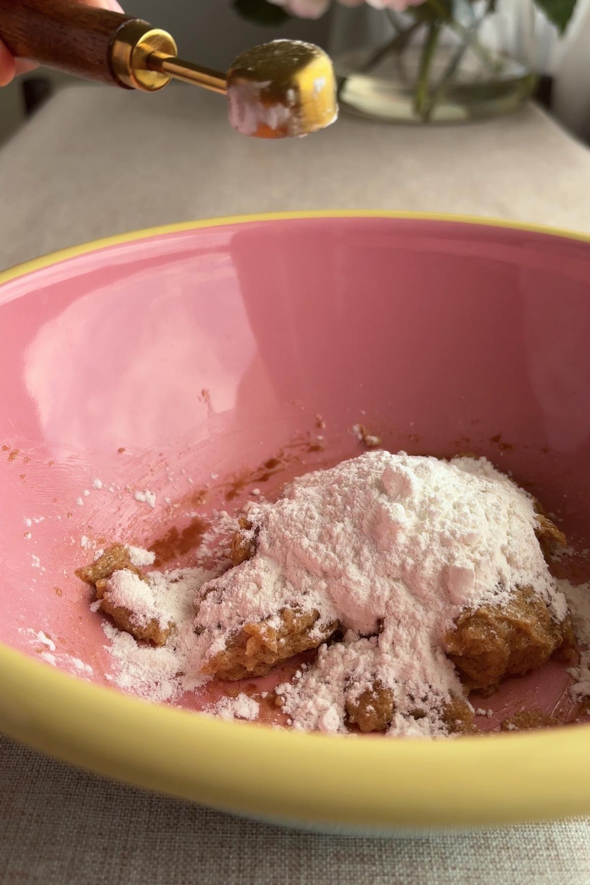 Flour and dry ingredients added to cookie dough mixture in a pink bowl.