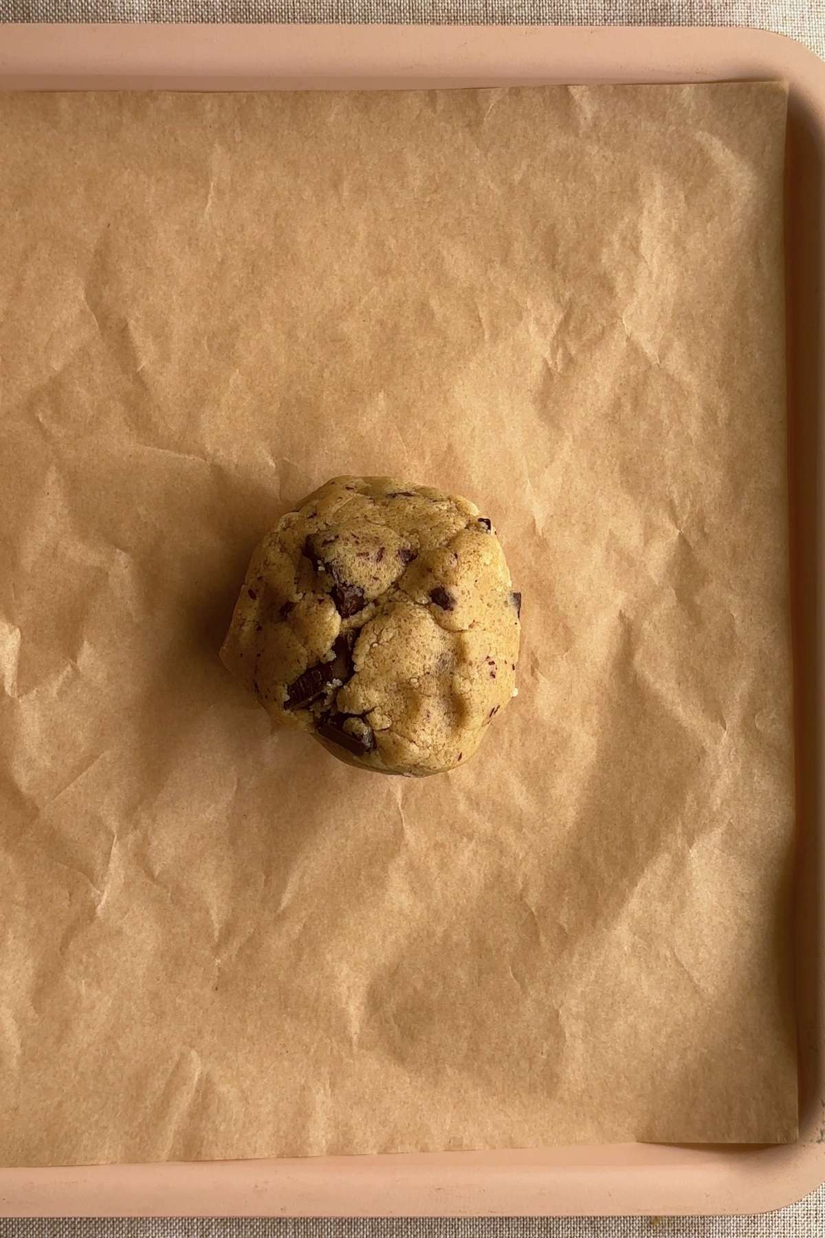 Cookie dough ball with chocolate chunks placed on parchment-lined tray.