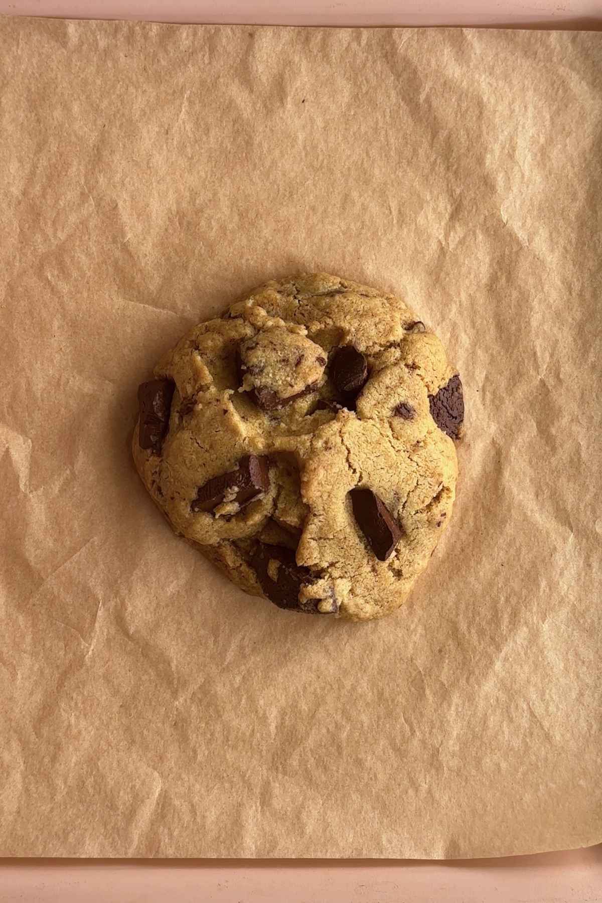 Golden-brown cookie with melted chocolate chunks on parchment paper.