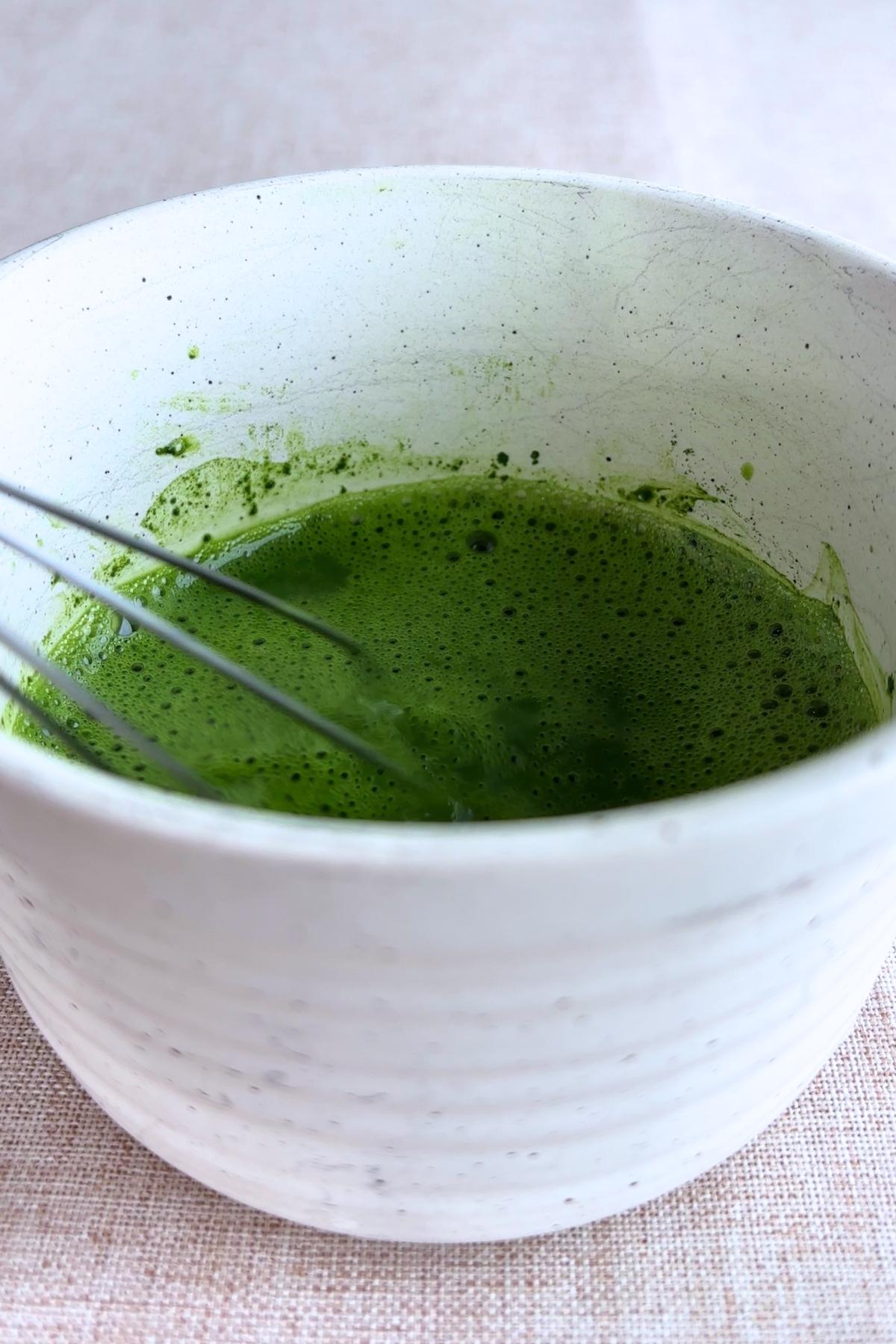 Whisked frothy green matcha tea in a white ceramic bowl.