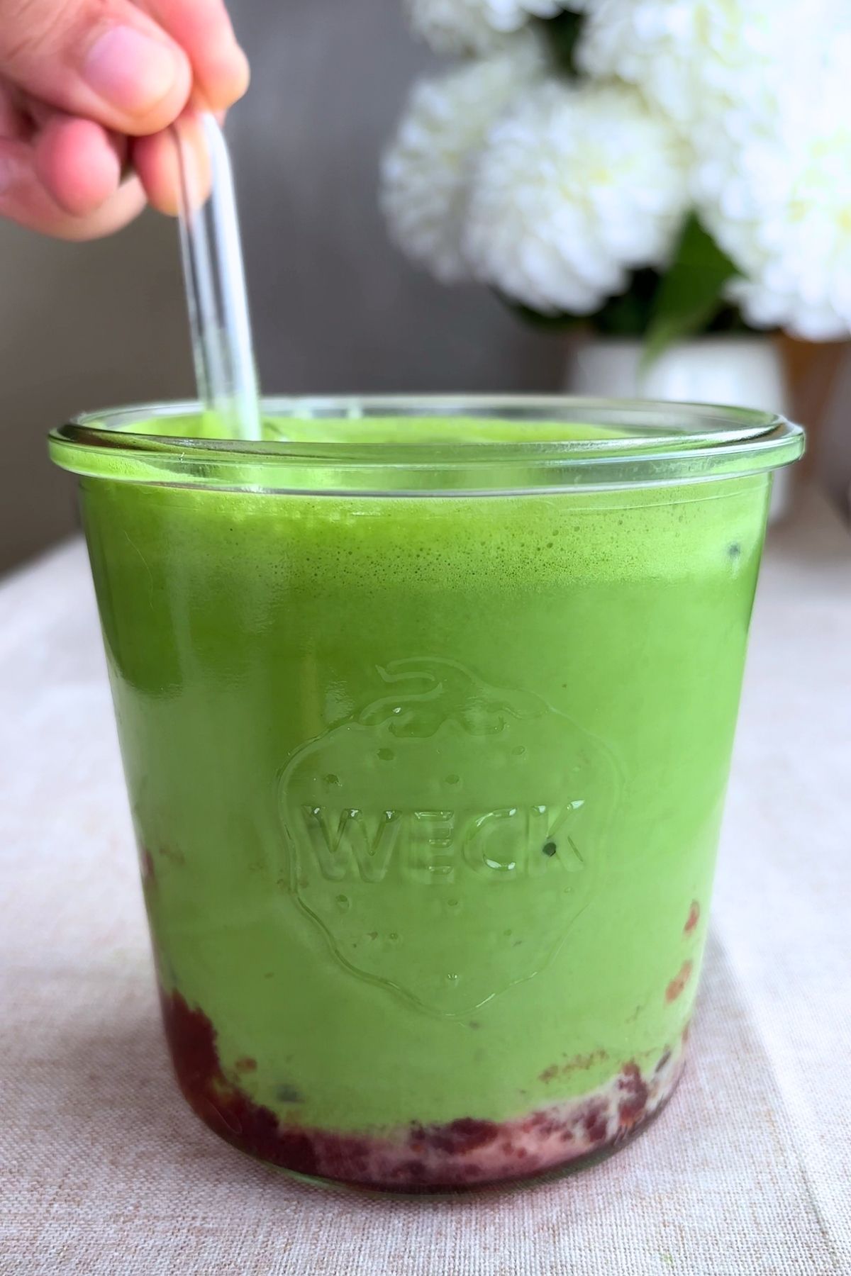 Strawberry, milk, and matcha layers combining in a clear glass with a straw.