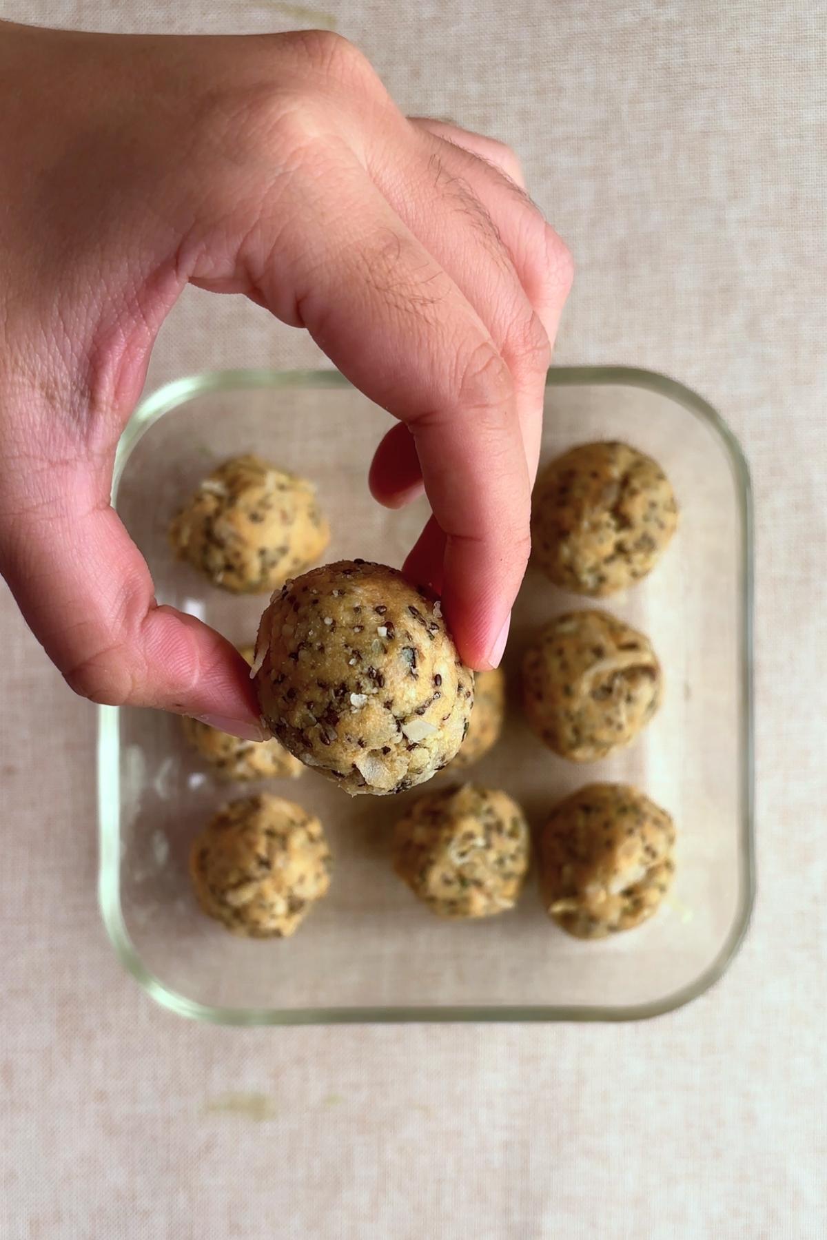 Hand holding a whole protein ball over the container.