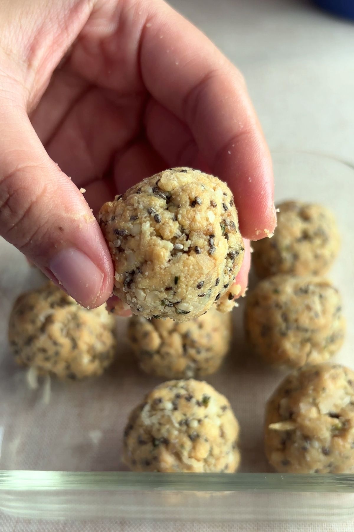 Close-up of a hand holding a protein ball with chia seeds and shredded coconut visible.