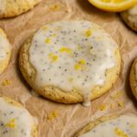 Cookies topped with lemon glaze and poppy seeds, sprinkled with lemon zest, with a lemon wedge nearby.