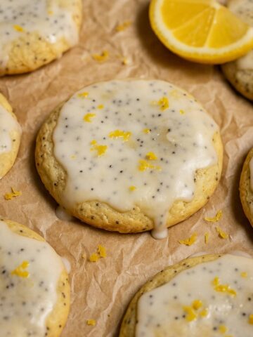 Cookies topped with lemon glaze and poppy seeds, sprinkled with lemon zest, with a lemon wedge nearby.
