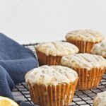 Close-up of glazed muffins on a cooling rack with a lemon wedge and navy cloth.