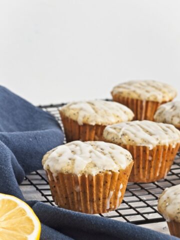 Close-up of glazed muffins on a cooling rack with a lemon wedge and navy cloth.