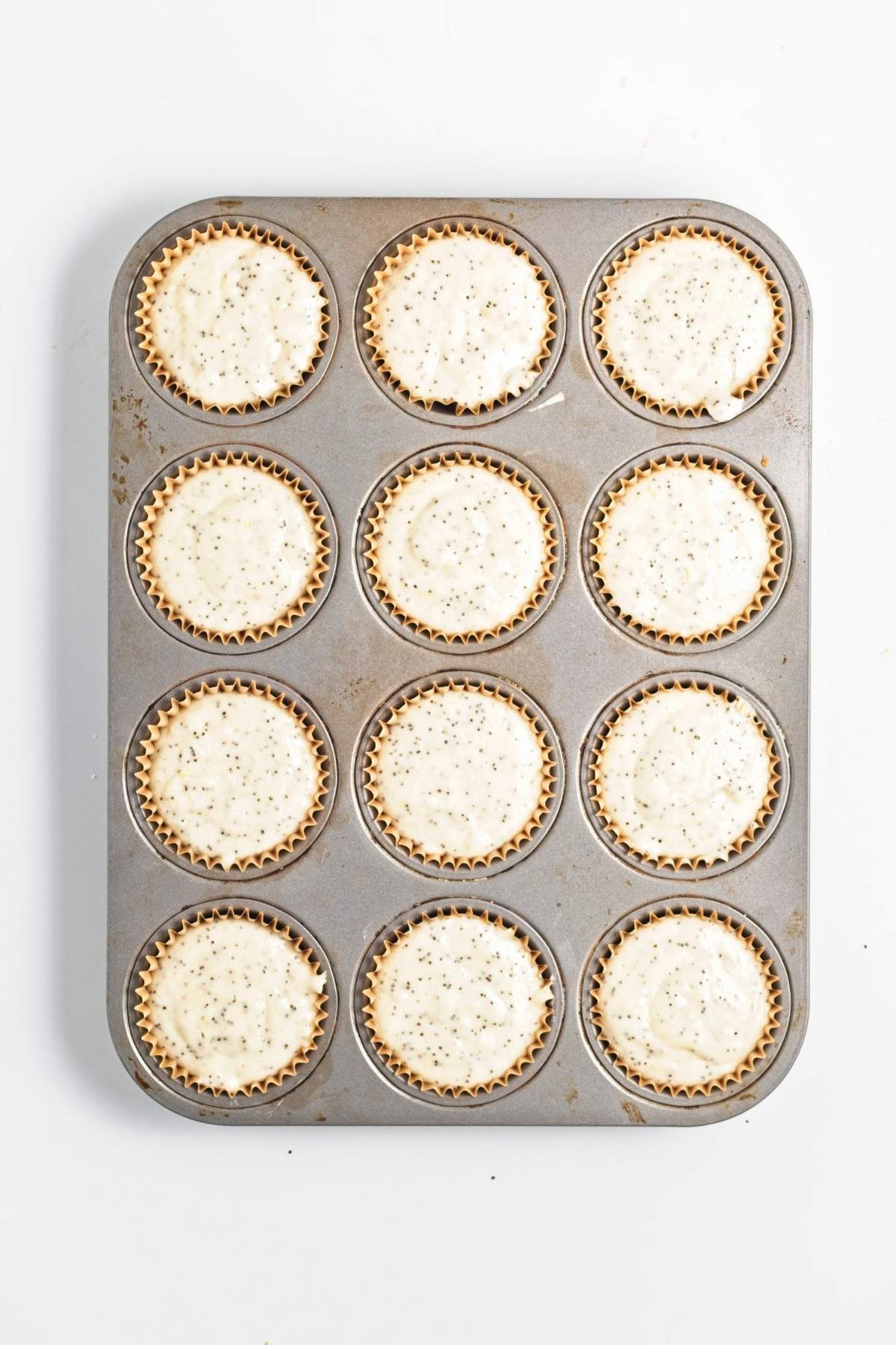Muffin tin lined with papers, each filled with speckled batter.