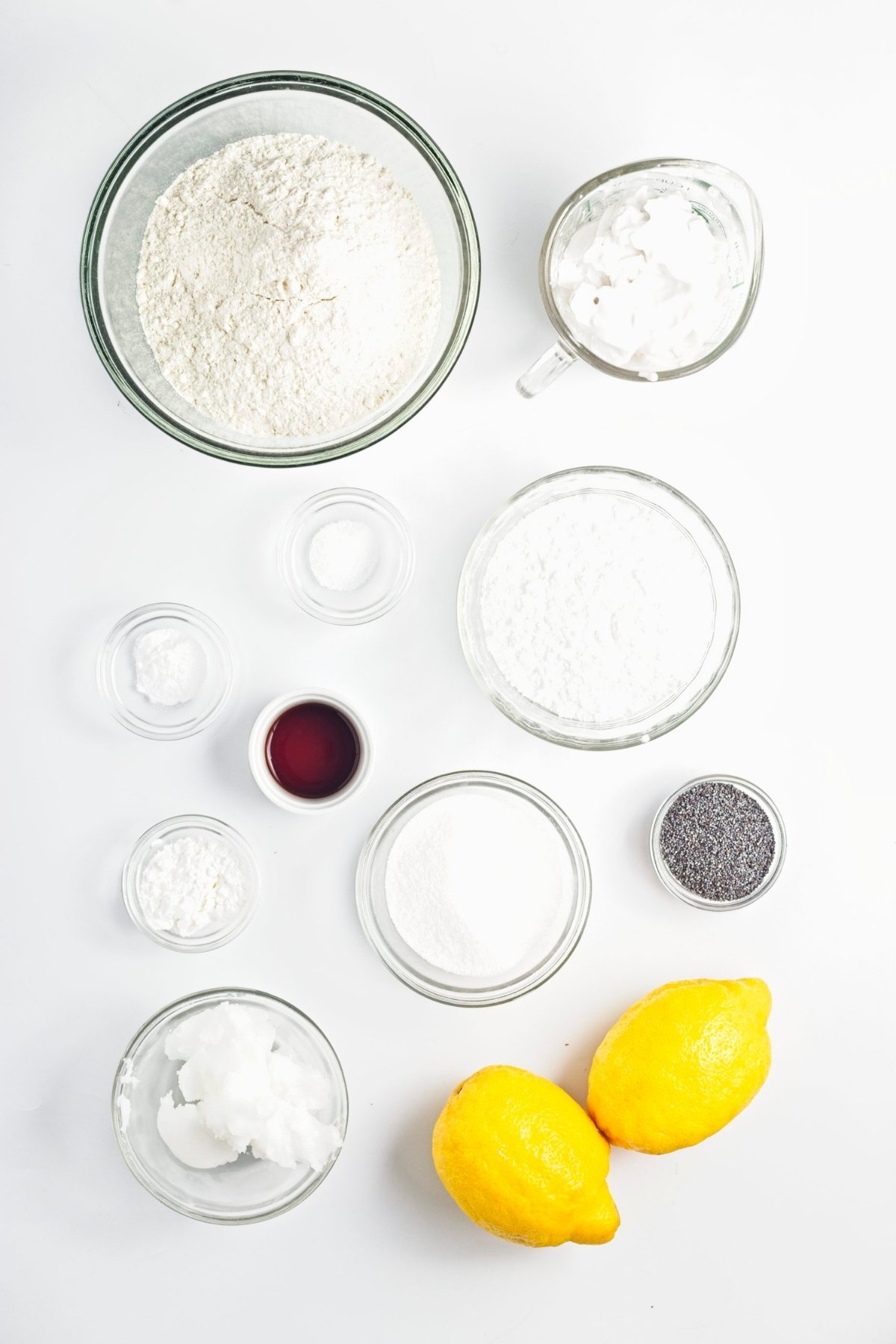 Measured baking ingredients including flour, sugar, coconut oil, lemons, and poppy seeds in glass bowls.