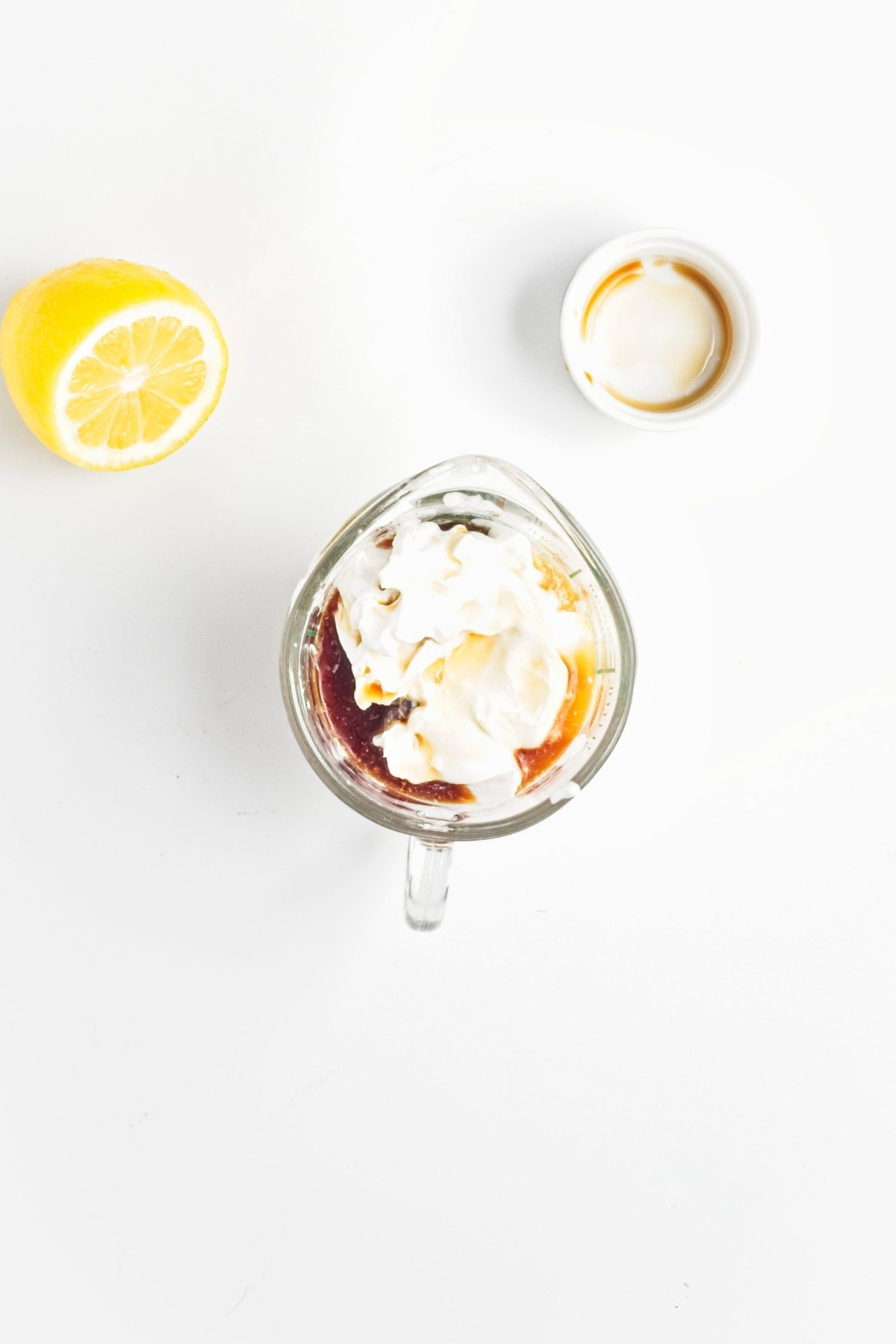 Measuring cup with coconut cream and vanilla, next to half a lemon and an empty ramekin.