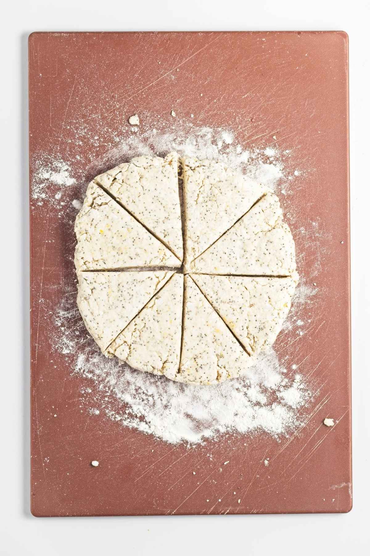 Round disc of scone dough with poppy seeds, cut into eight wedges on a floured board.