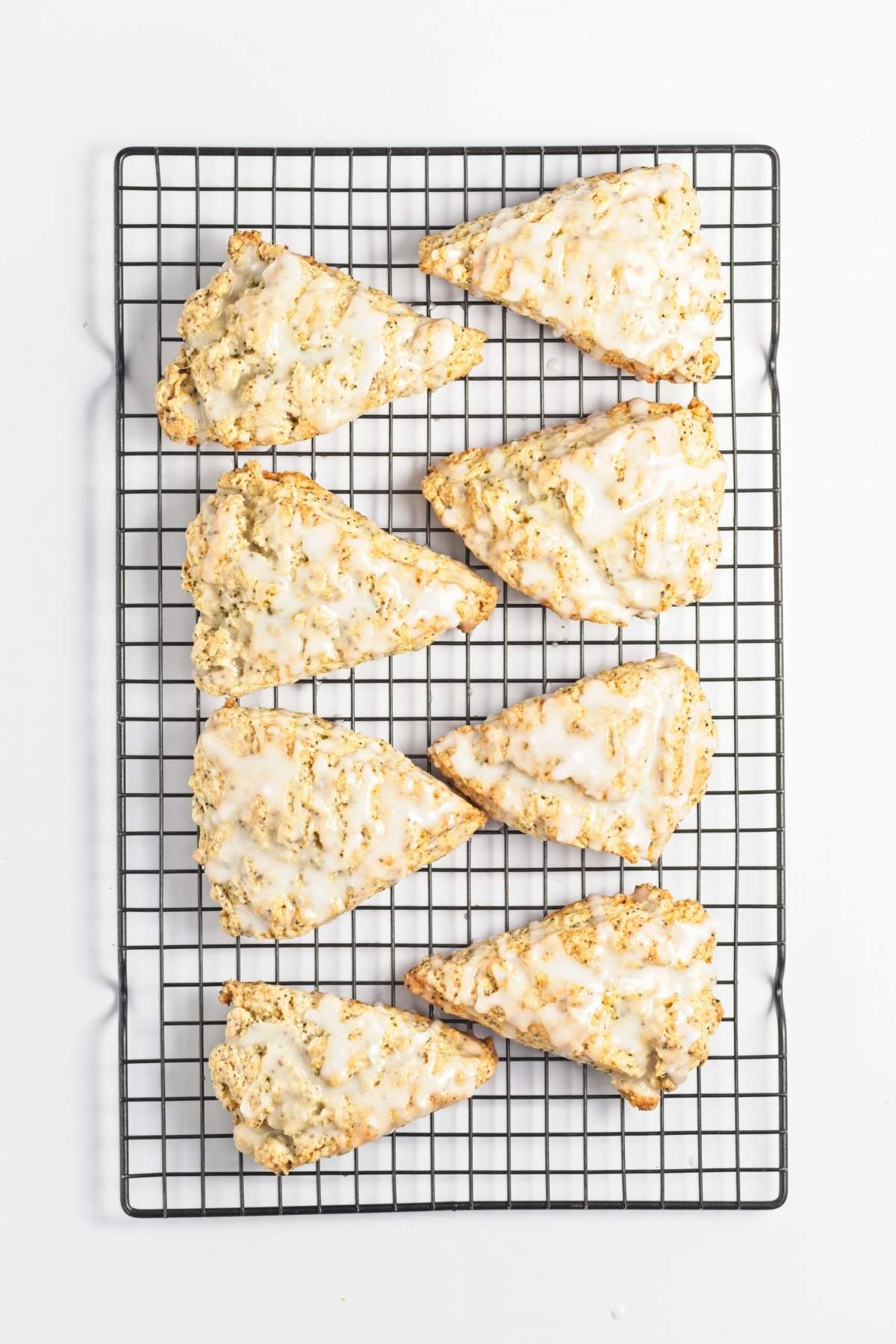 Eight glazed scones cooling on a black wire rack.