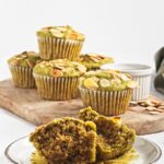 Halved green muffin on a plate with more muffins in the background on a wooden board.