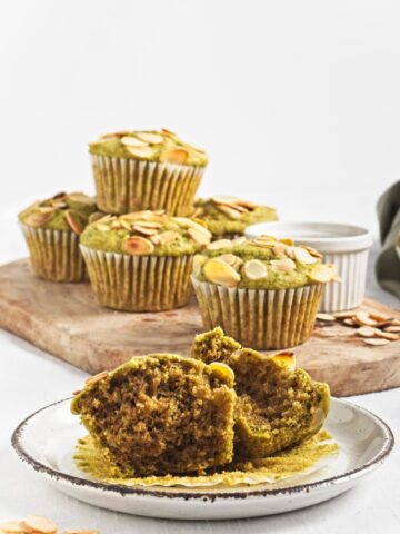 Halved green muffin on a plate with more muffins in the background on a wooden board.