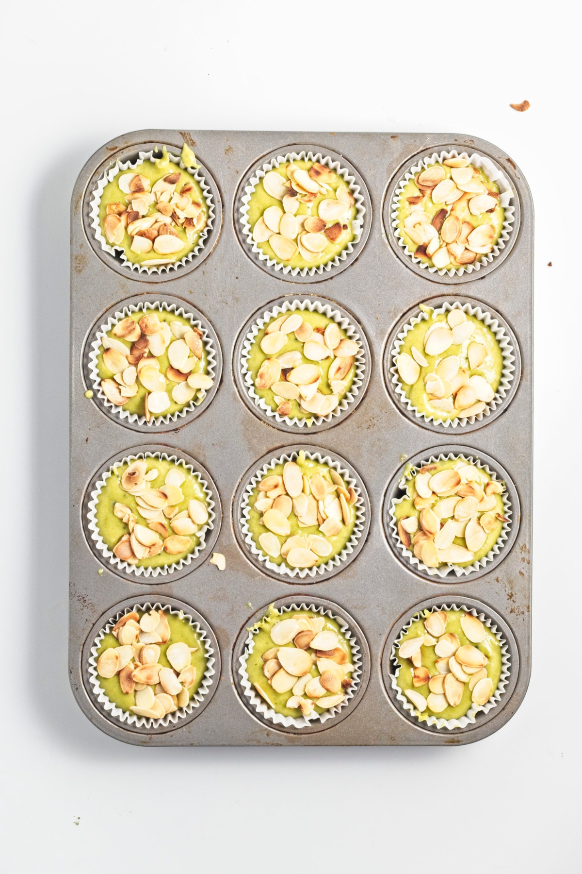 Paper-lined muffin tin with green batter topped with sliced almonds.