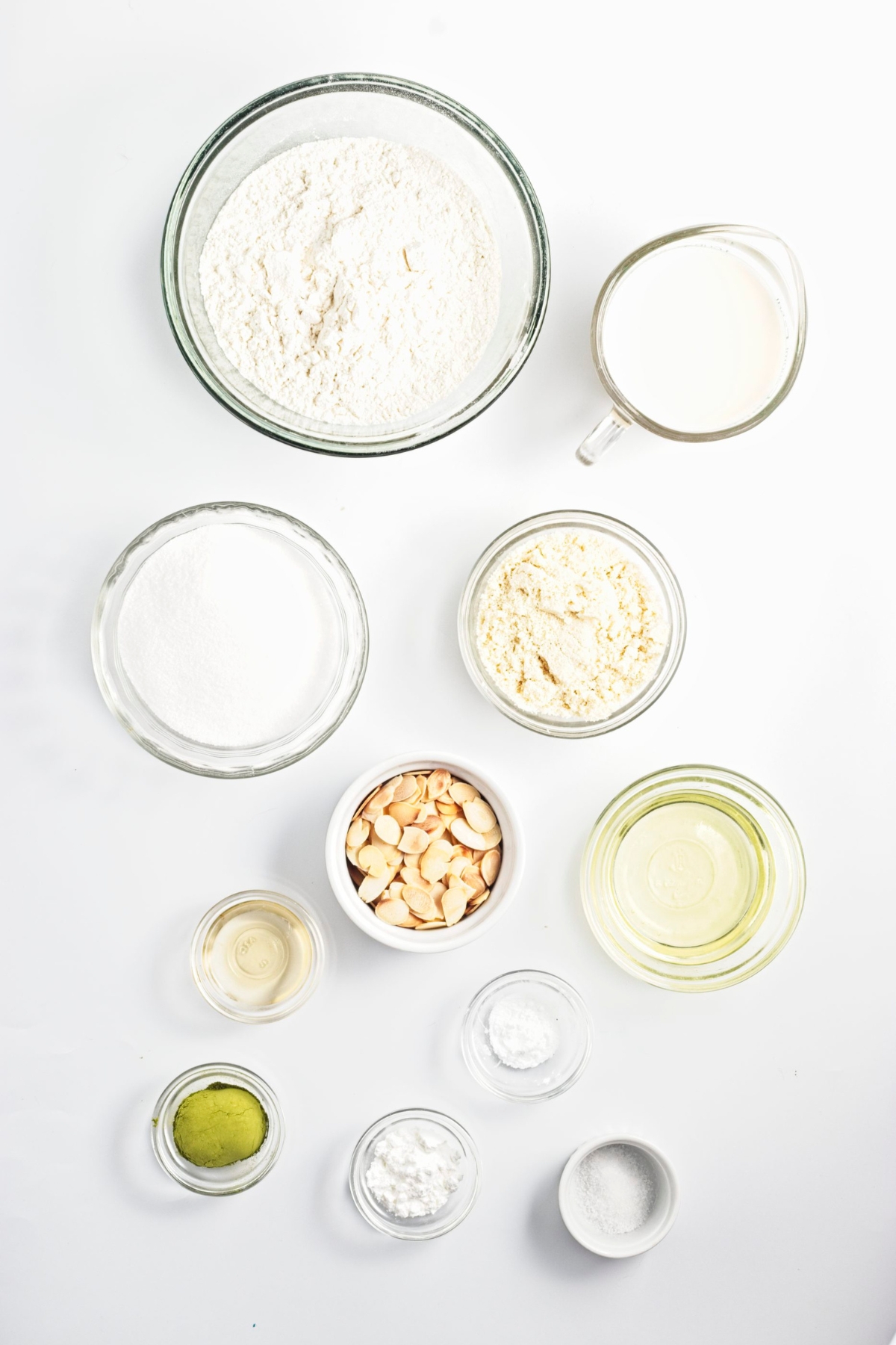 Measured ingredients in bowls and cups arranged on a white surface.
