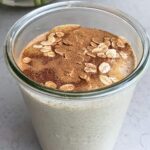 Smoothie in a glass jar topped with peanut butter drizzle, oats and cinnamon dust.