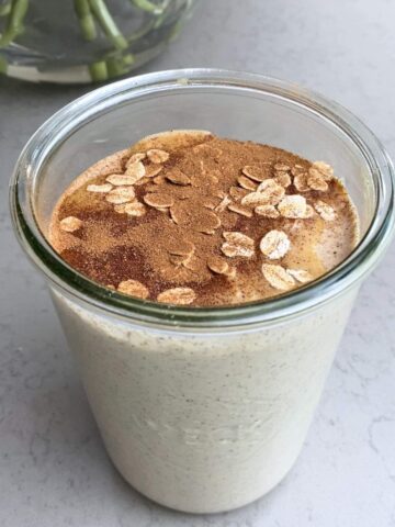 Smoothie in a glass jar topped with peanut butter drizzle, oats and cinnamon dust.