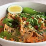 Close-up of dumpling soup topped with sesame seeds, cilantro, and lime wedge.