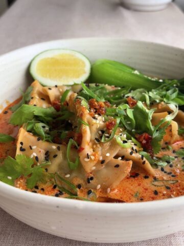 Close-up of dumpling soup topped with sesame seeds, cilantro, and lime wedge.