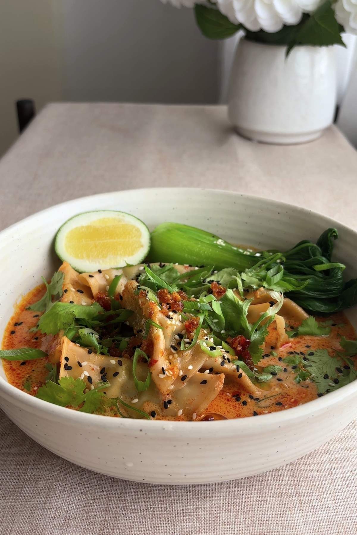 Side view of dumpling soup with bok choy and lime wedge.
