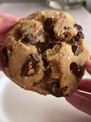 Hands holding a thick cookie with visible melted chocolate chunks.