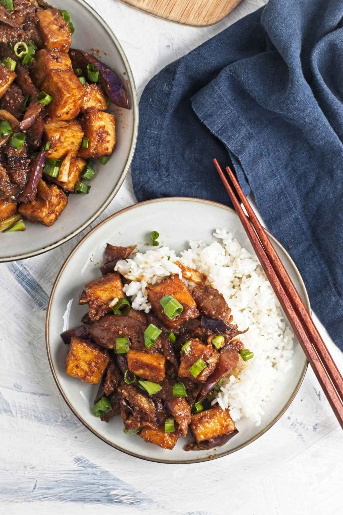 Bowl of saucy tofu and eggplant served with white rice, topped with chopped green onions.