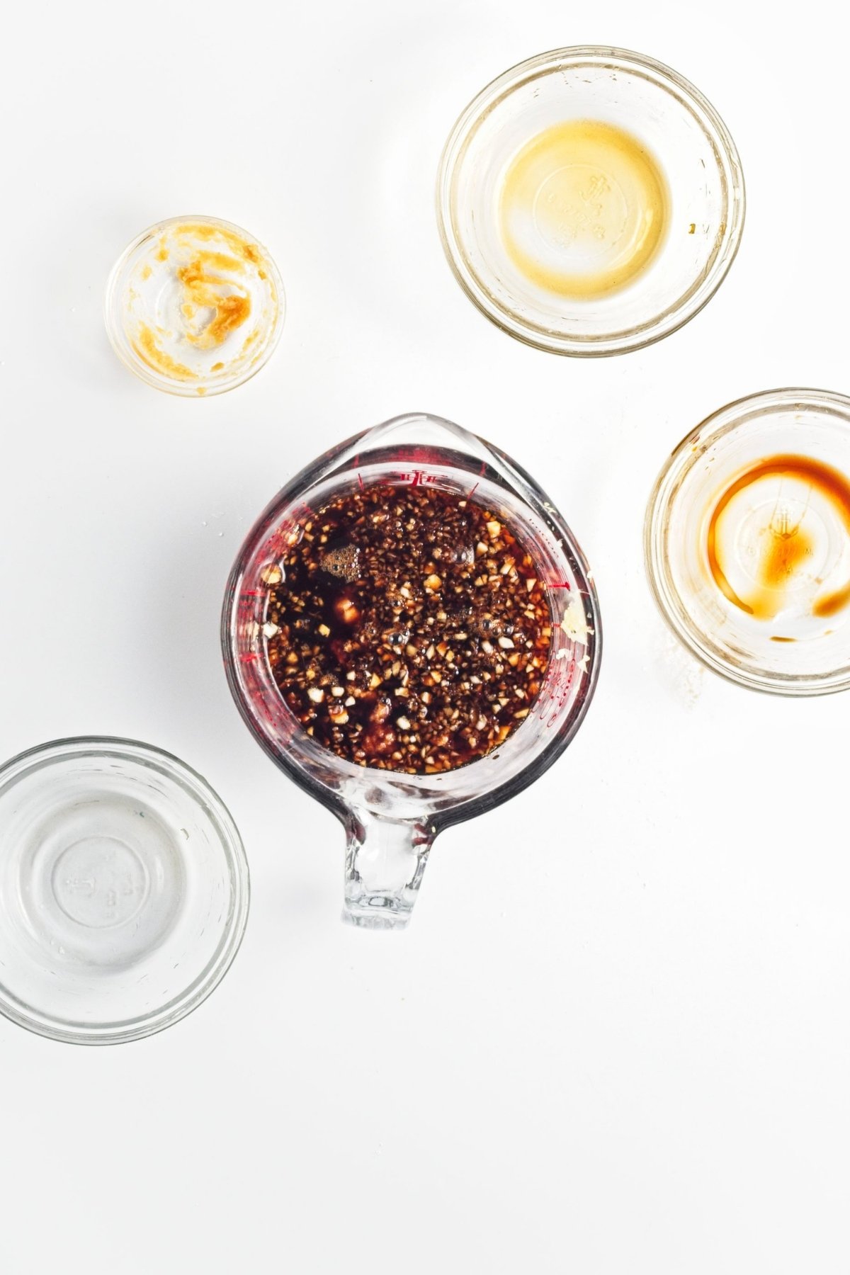 Dark soy-based sauce mixture with minced garlic and ginger in a measuring jug, surrounded by used small bowls.