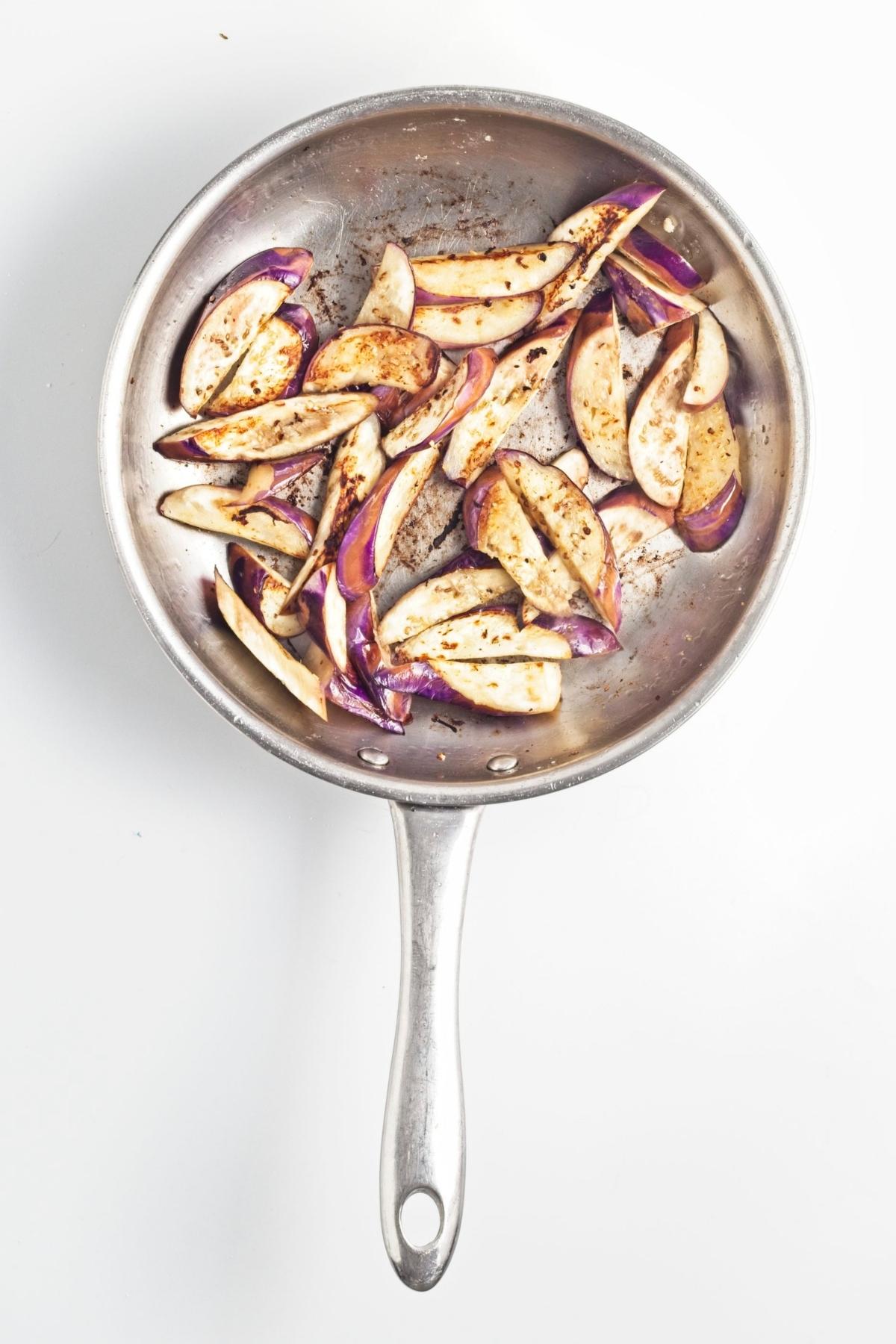 Sliced eggplant pieces browning in a stainless steel pan.