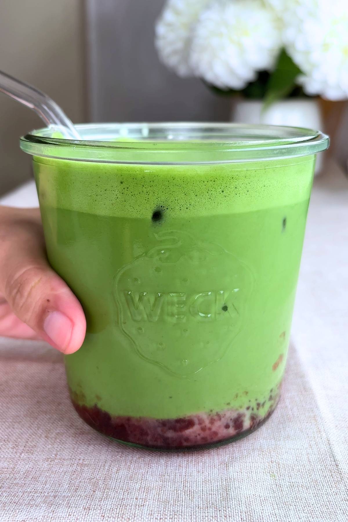 Layered strawberry matcha latte in a clear glass jar with visible jam at the base.
