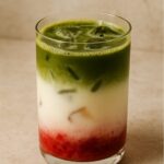 Layered iced drink with red fruit base, white milk center, and green matcha top.