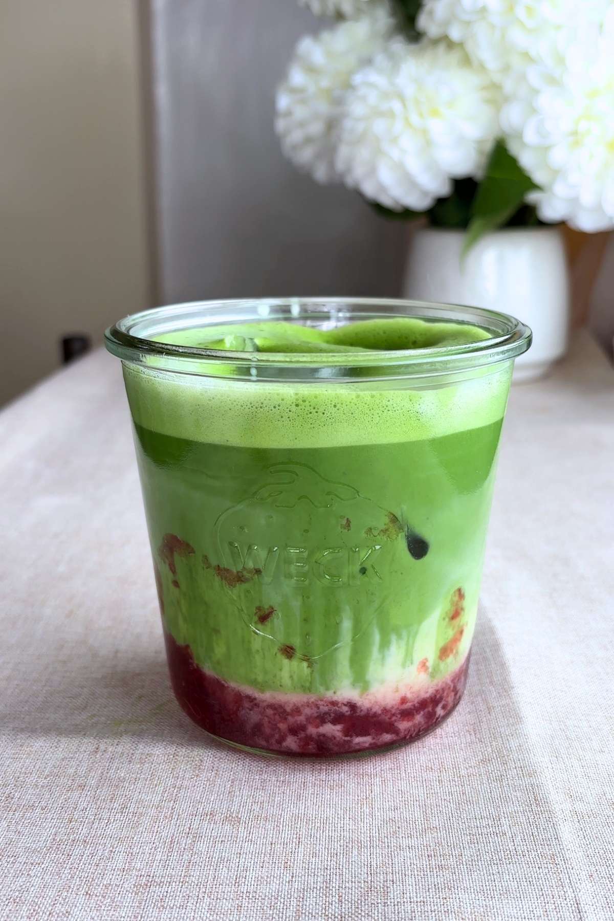 Strawberry matcha latte in a glass, showing bright green layers over red jam.
