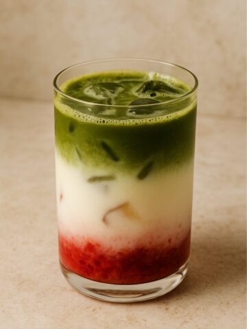 Layered iced drink with red fruit base, white milk center, and green matcha top.