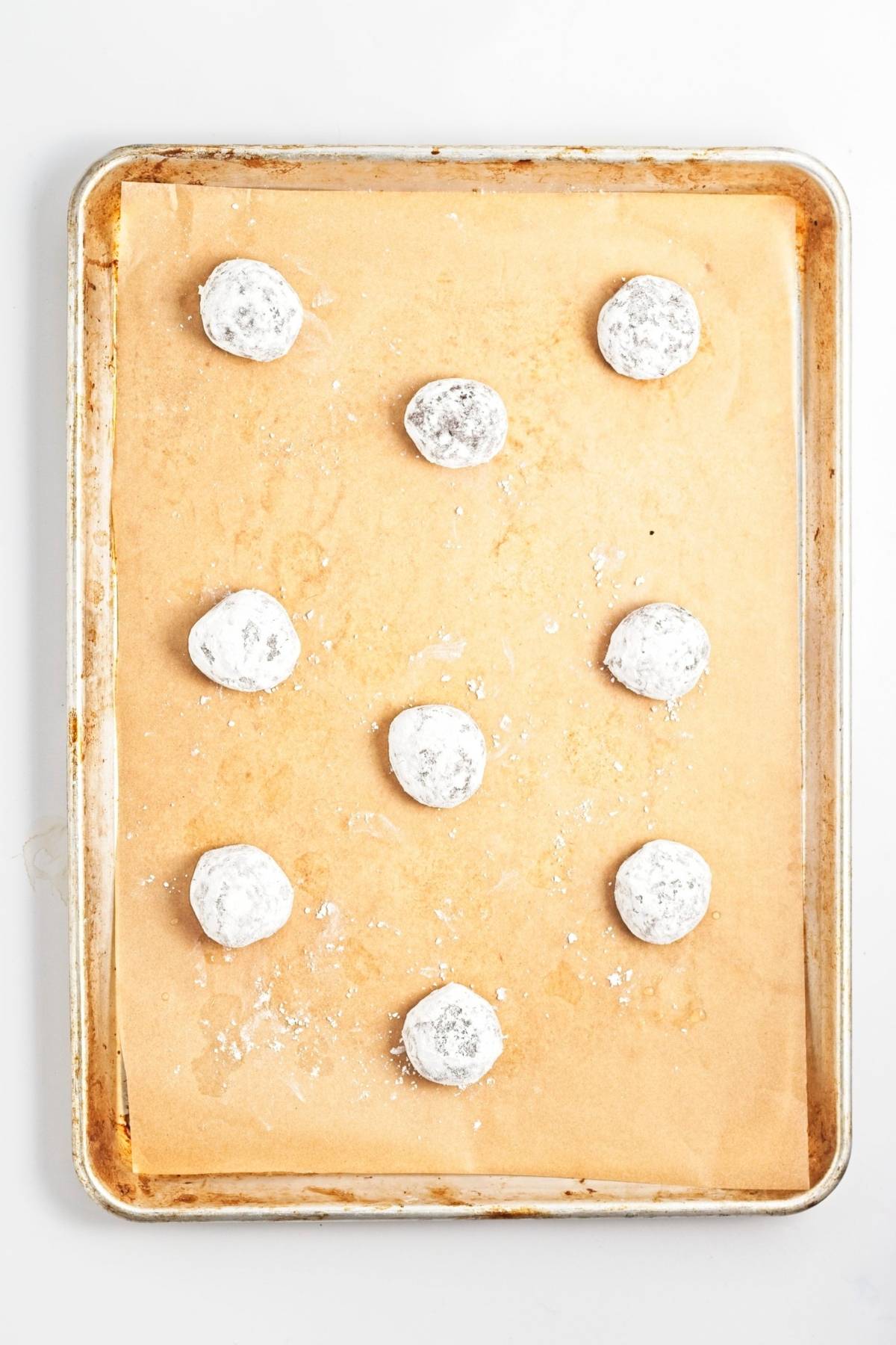 Chocolate cookie dough balls coated in powdered sugar, arranged on a parchment-lined baking sheet before baking.