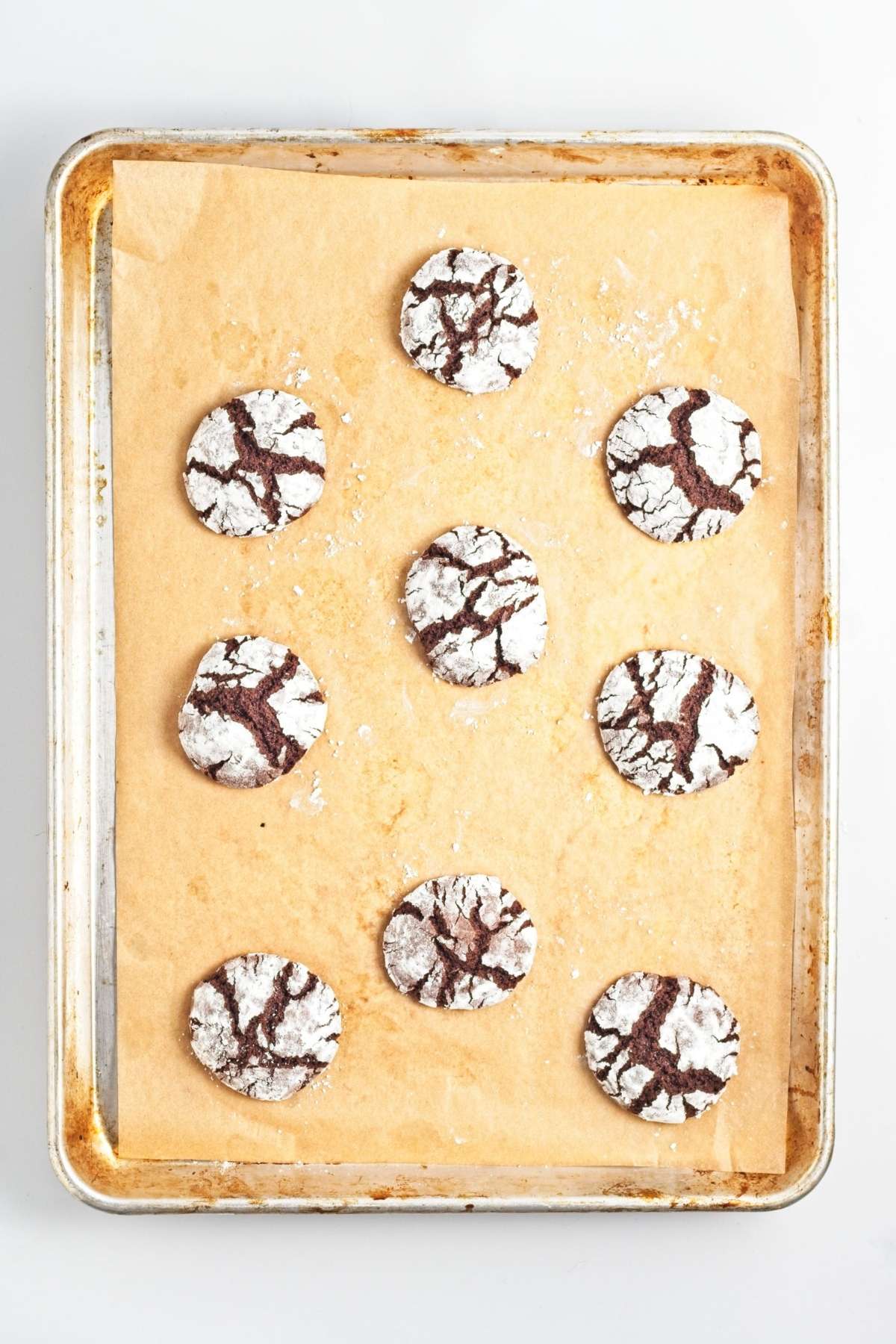 Baked chocolate crinkle cookies with cracked powdered sugar tops on parchment-lined baking sheet.