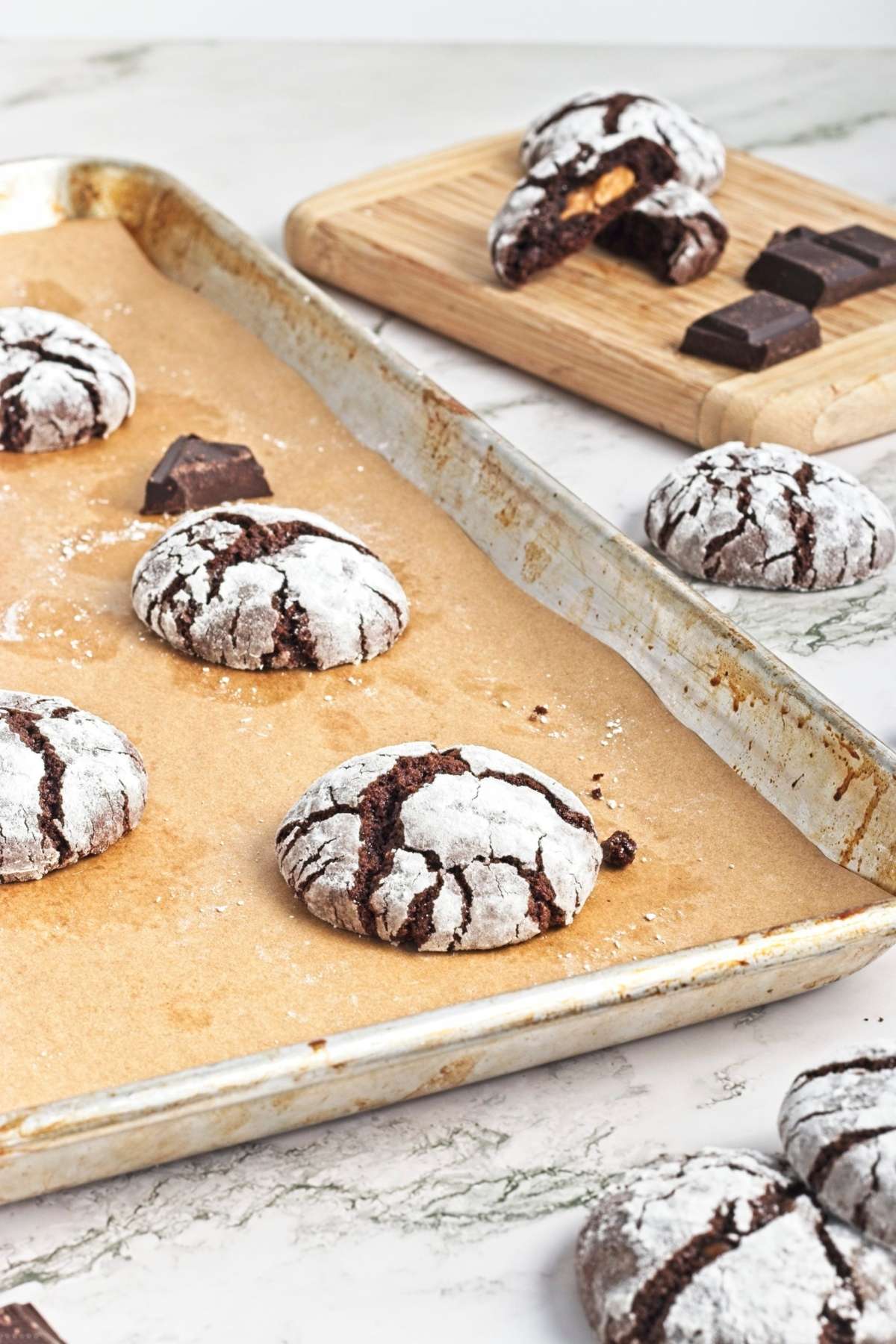 Freshly baked crinkle cookies on a parchment-lined baking sheet with chocolate pieces.