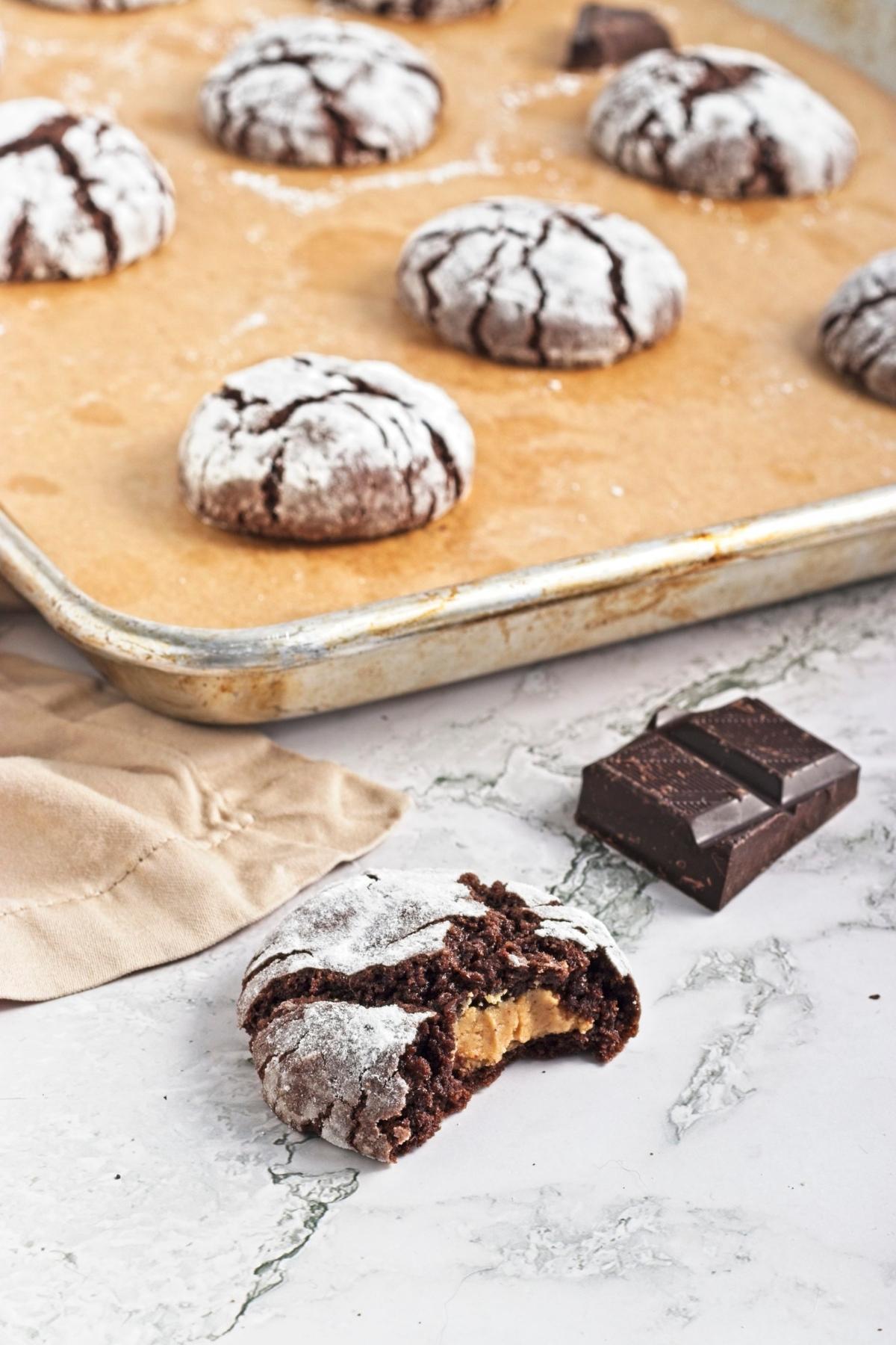 Overhead view of cookies on a baking sheet with extra chocolate pieces and cookies on a wooden board.
