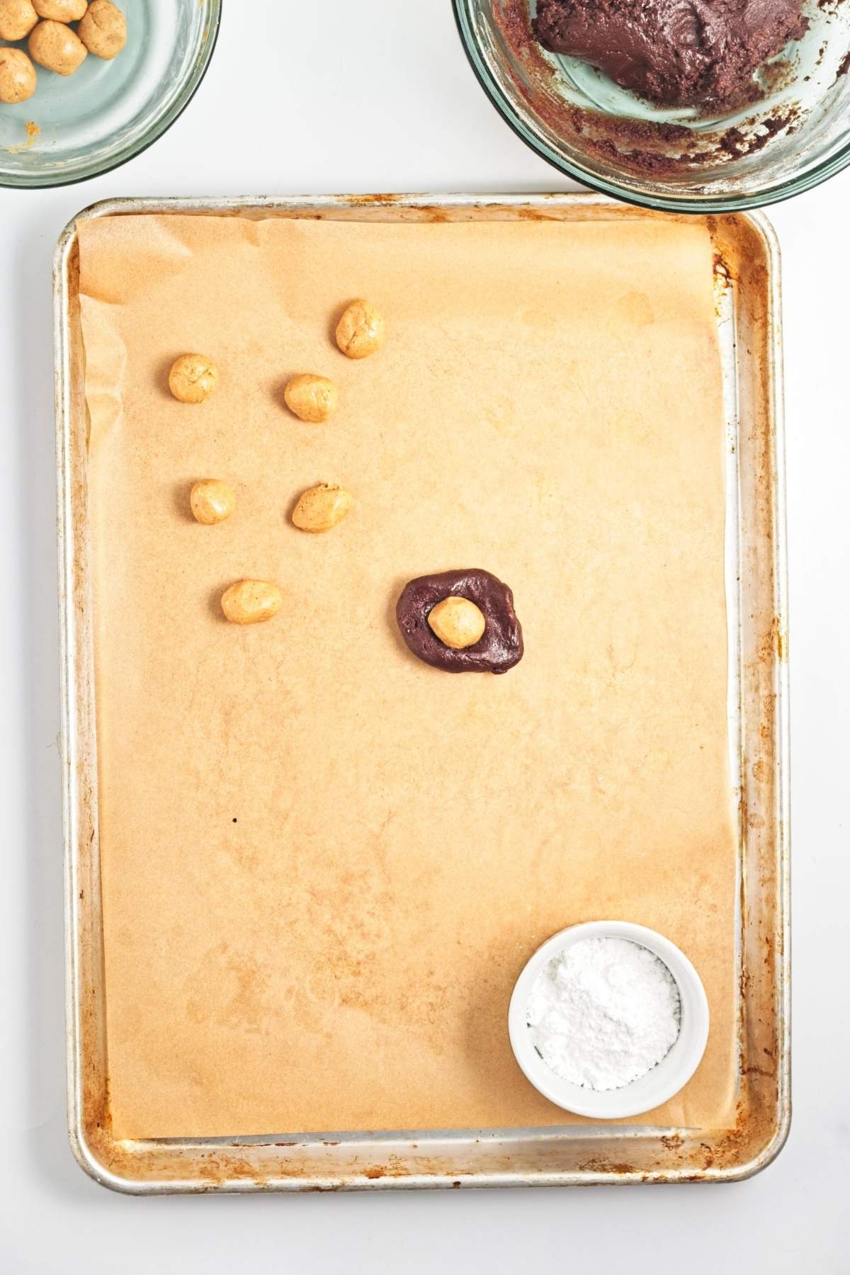 Peanut butter balls on baking sheet, with one chocolate-covered ball sitting in a bowl of powdered sugar.