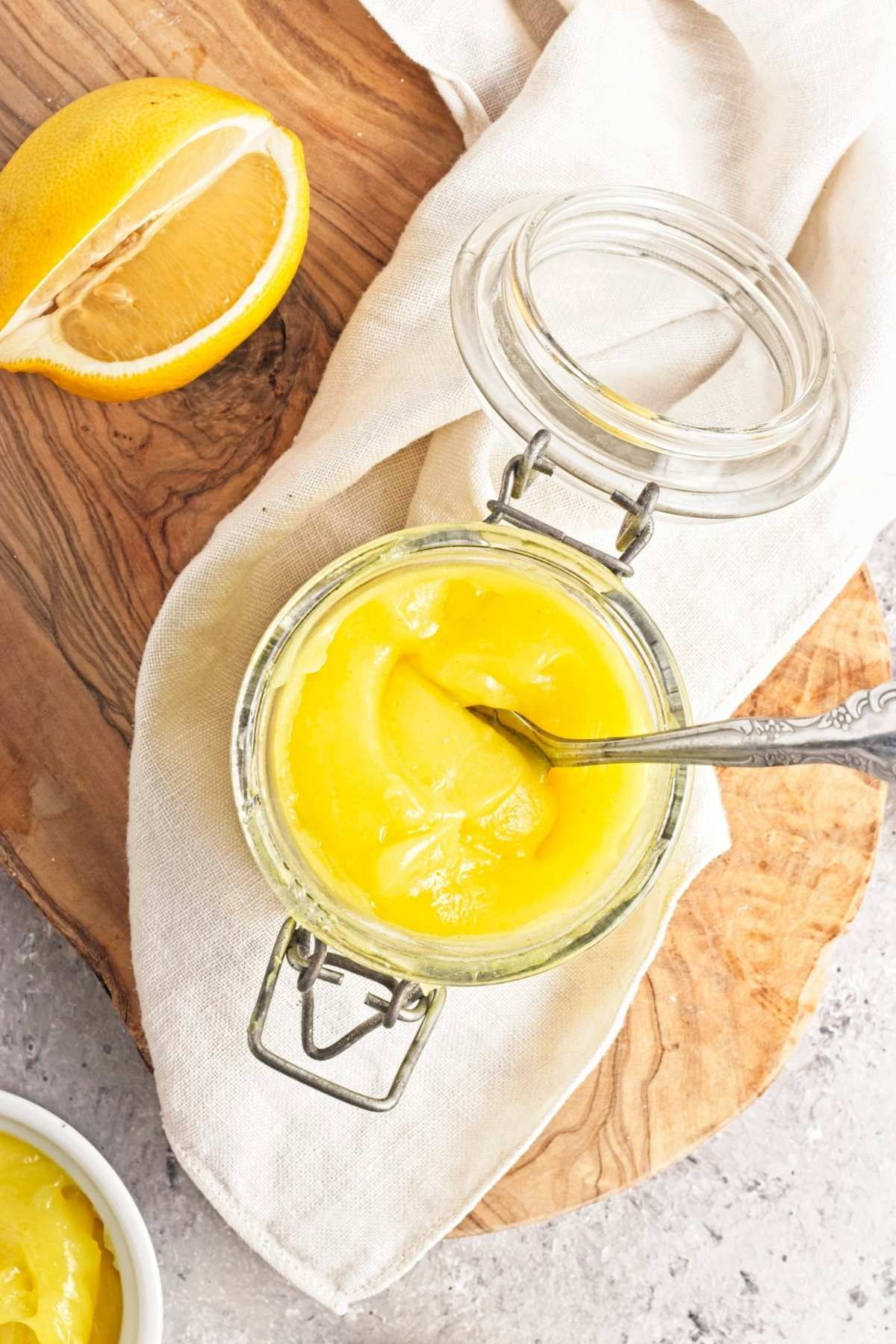 Spoon in a jar of thick yellow curd with a halved lemon beside it.