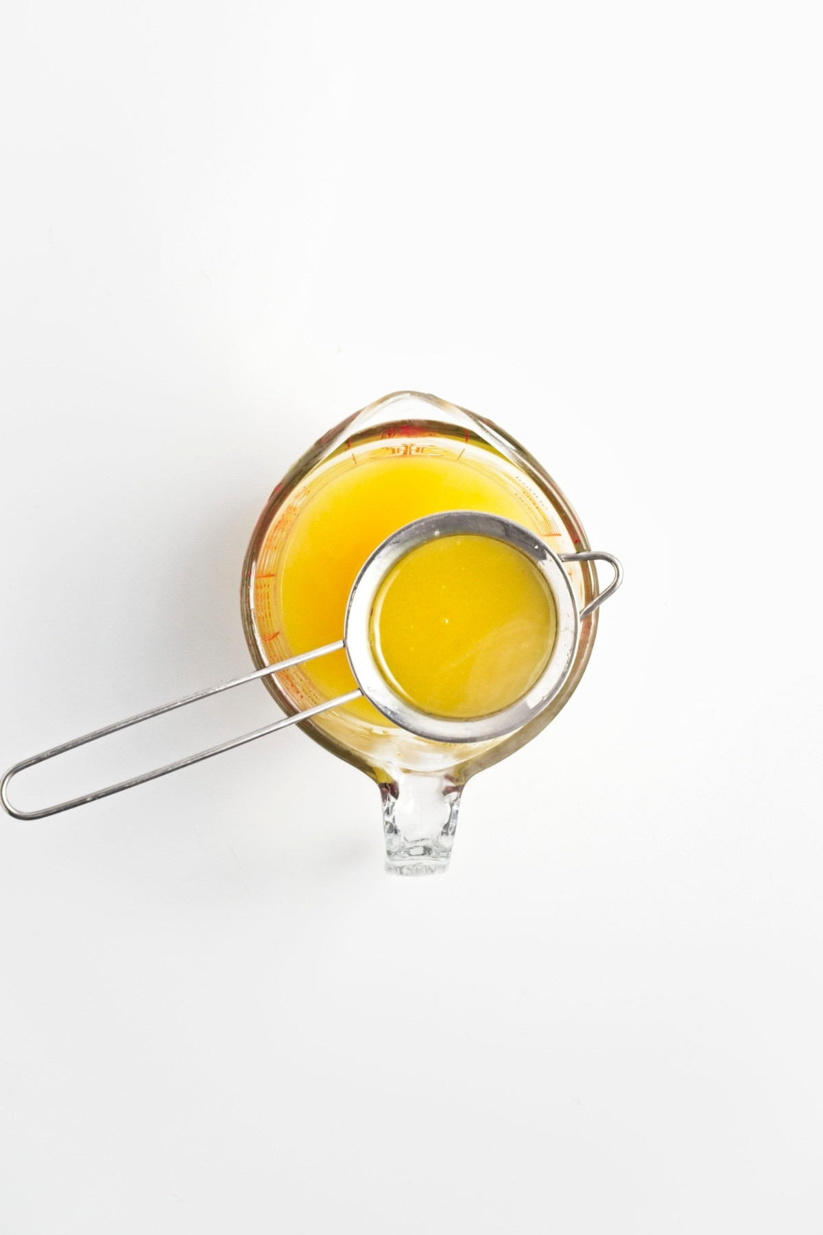Measuring jug with lemon curd and fine mesh strainer on top.