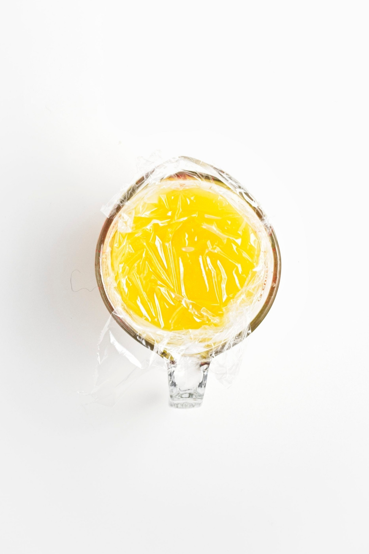Measuring jug of lemon curd covered with plastic wrap.